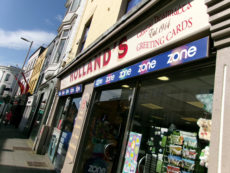 Storefront with 'Holland's' greeting cards branding on a sunny day.